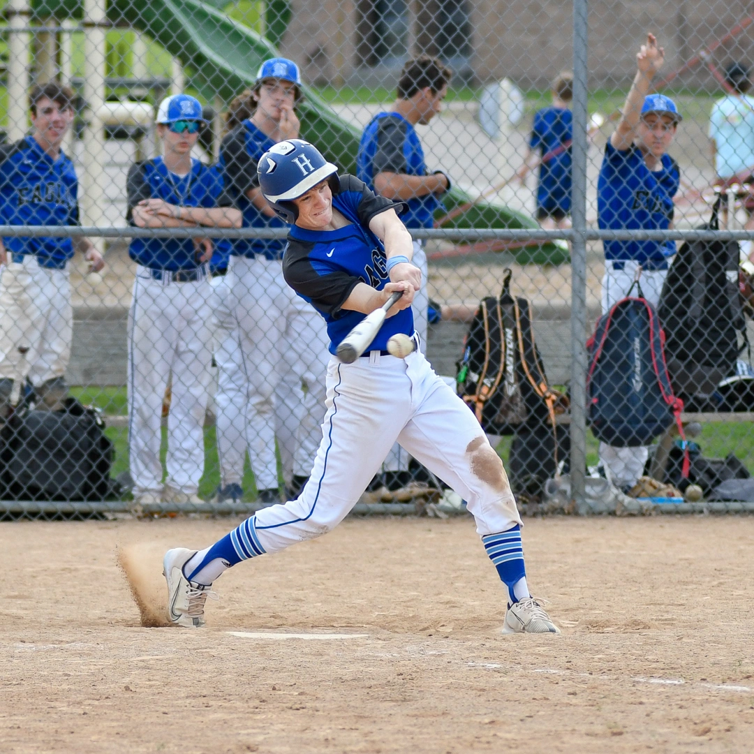 High school baseball player makes contact at the plate with teammates watching from the dugout during a Minnesota game day