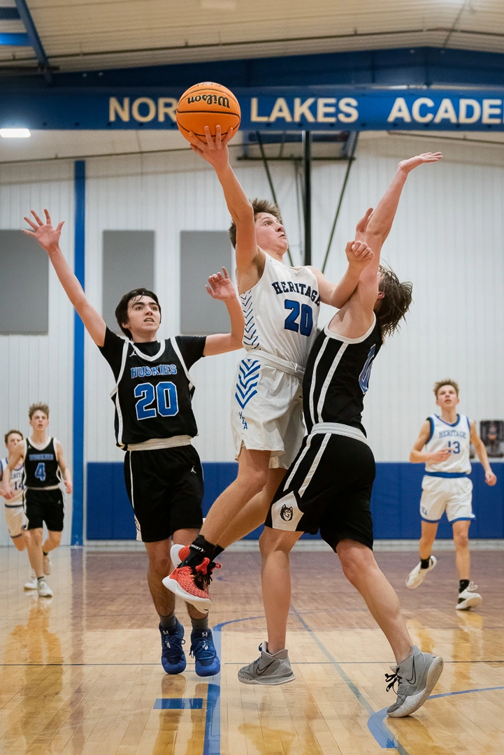 High school basketball player drives between two Huskies defenders for a layup during a Minnesota high school game