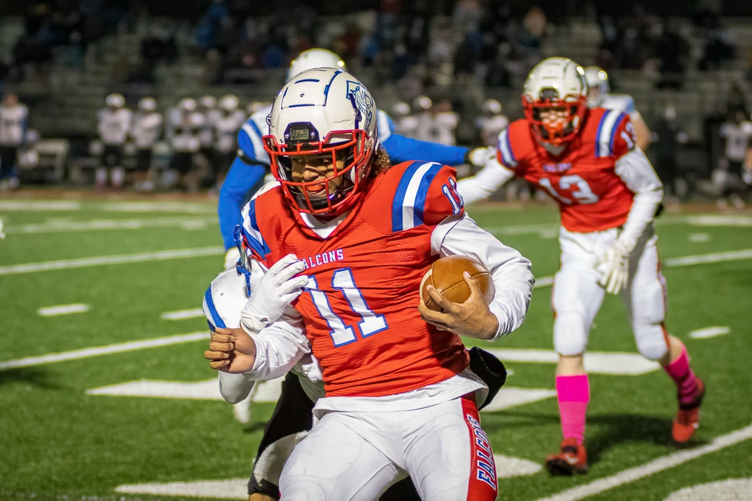 Armstrong Falcons high school football player breaks a tackle and drives forward during a Minnesota night game
