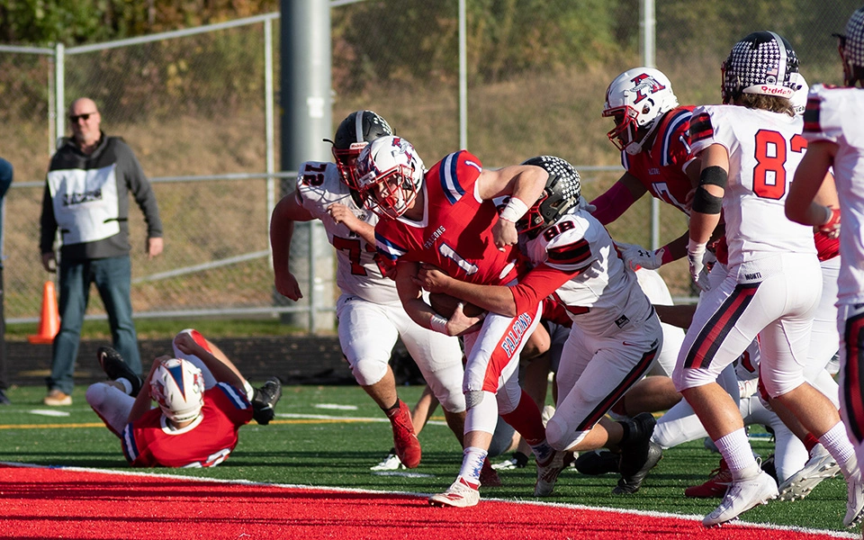 High school football player scoring a touchdown while defender tries to tackle him at the goal line