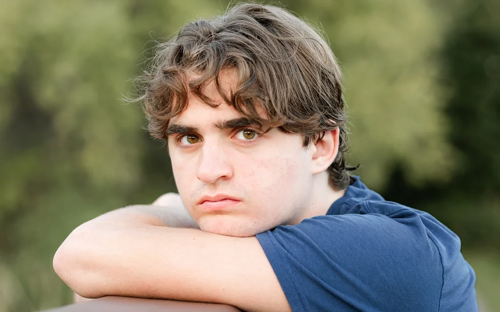 Moody close-up senior portrait of high school boy leaning on arms outdoors with natural green background — Plymouth Minnesota