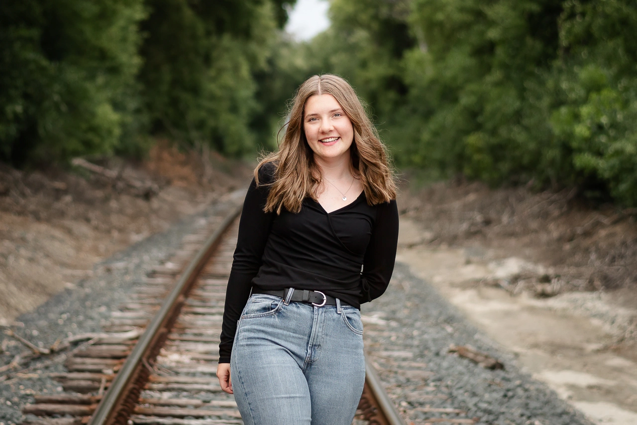 High school senior girl walks on railroad tracks in black top and jeans — Golden Valley Minnesota senior portrait photographer