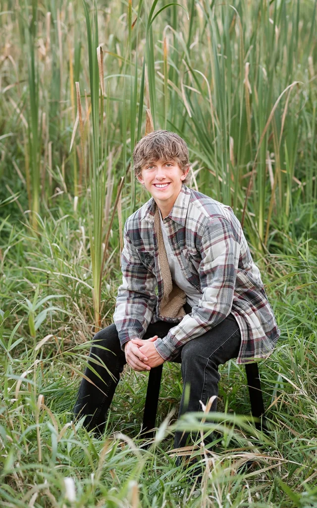 Heritage Christian Academy high school senior guy sits on stool among tall cattails in plaid flannel — Twin Cities senior portrait photography
