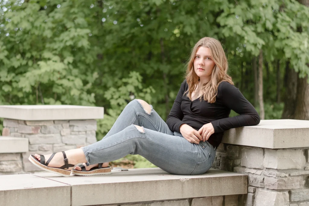 High school senior girl reclines on stone ledge in black top and ripped jeans — Plymouth Minnesota senior portrait photographer