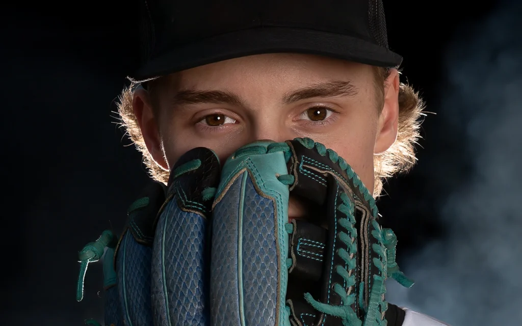 Creative baseball sports portrait of Twin Cities athlete holding glove over face with dramatic studio lighting
