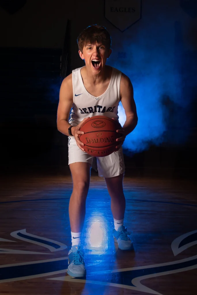 High school boys basketball player yells with intensity holding Spalding ball with dramatic blue smoke lighting — Twin Cities Sportraits photography