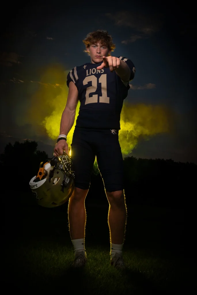 Providence Lions high school football player points at camera holding helmet with dramatic yellow smoke background — Twin Cities Sportraits photography