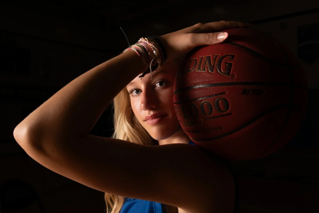 Dramatic girls basketball sports portrait with player holding Spalding ball beside face — Twin Cities athlete photography