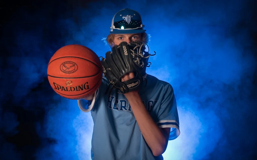 Dual-sport high school athlete holds basketball and baseball glove in dramatic blue smoke sports portrait — Minneapolis Minnesota