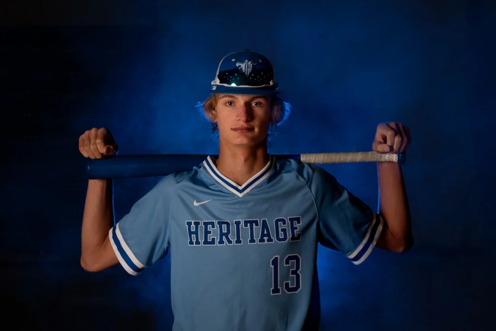 High school baseball player holds bat across shoulders in dramatic blue smoke sports portrait — Maple Grove athlete photography