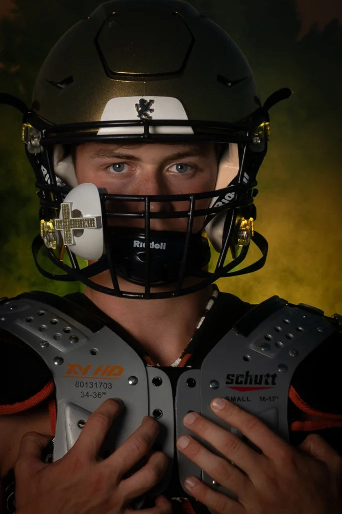 Intense close-up sports portrait of Plymouth Minnesota high school football player in helmet and shoulder pads with yellow fog background