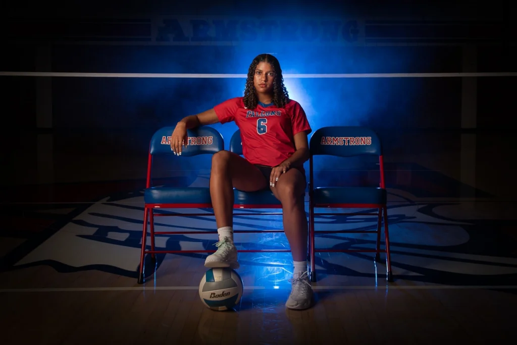 Armstrong Falcons volleyball player sits on team bench with foot on ball and dramatic blue smoke lighting — Twin Cities Sportraits photography