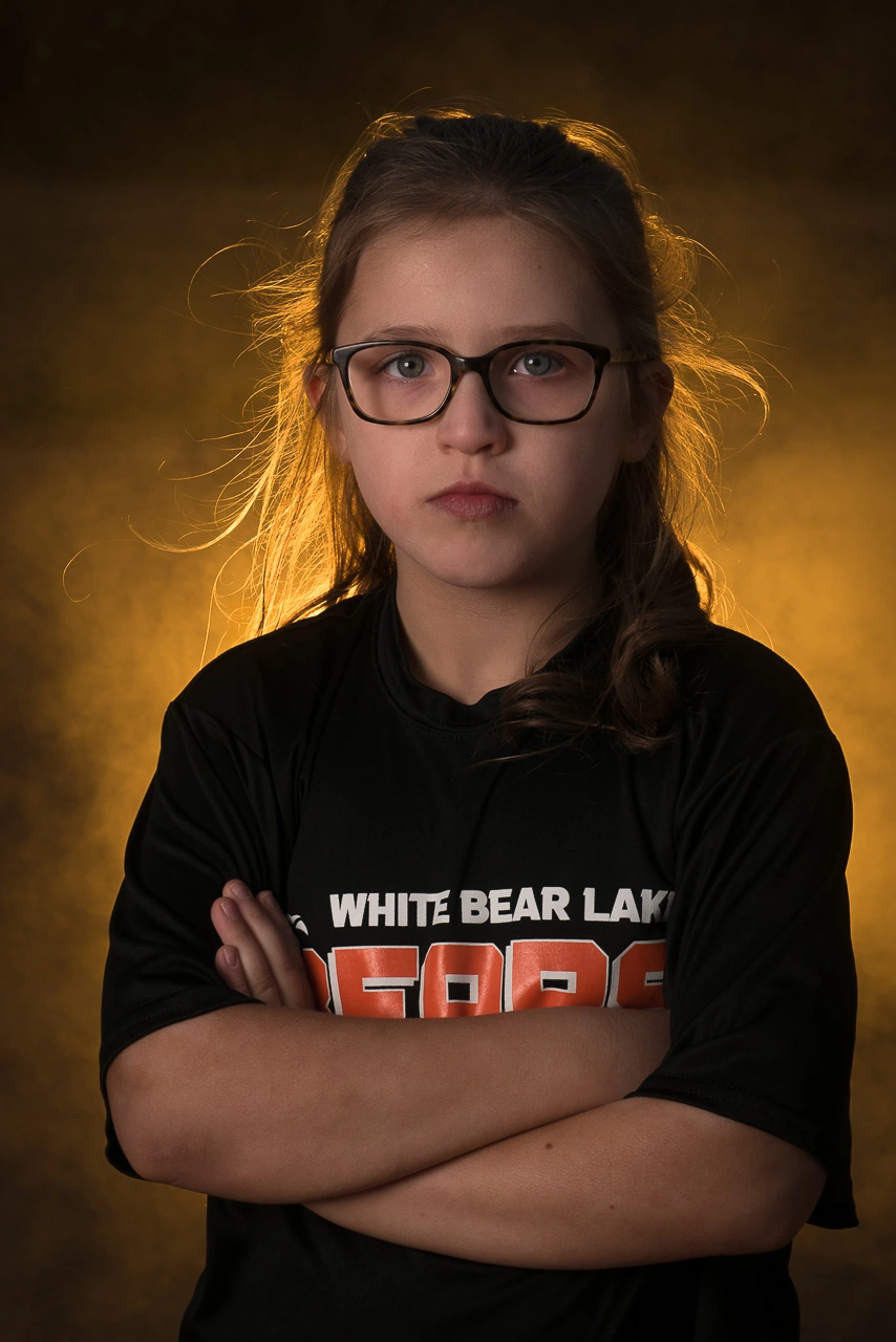 Dramatic sports portrait of White Bear Lake Bears softball player with arms crossed and golden smoke background — Twin Cities athlete photography