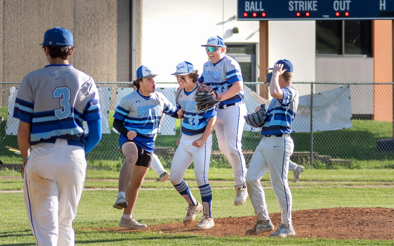 Heritage baseball teammates rush the mound to celebrate a pitcher's win during a Minnesota high school baseball playoff game