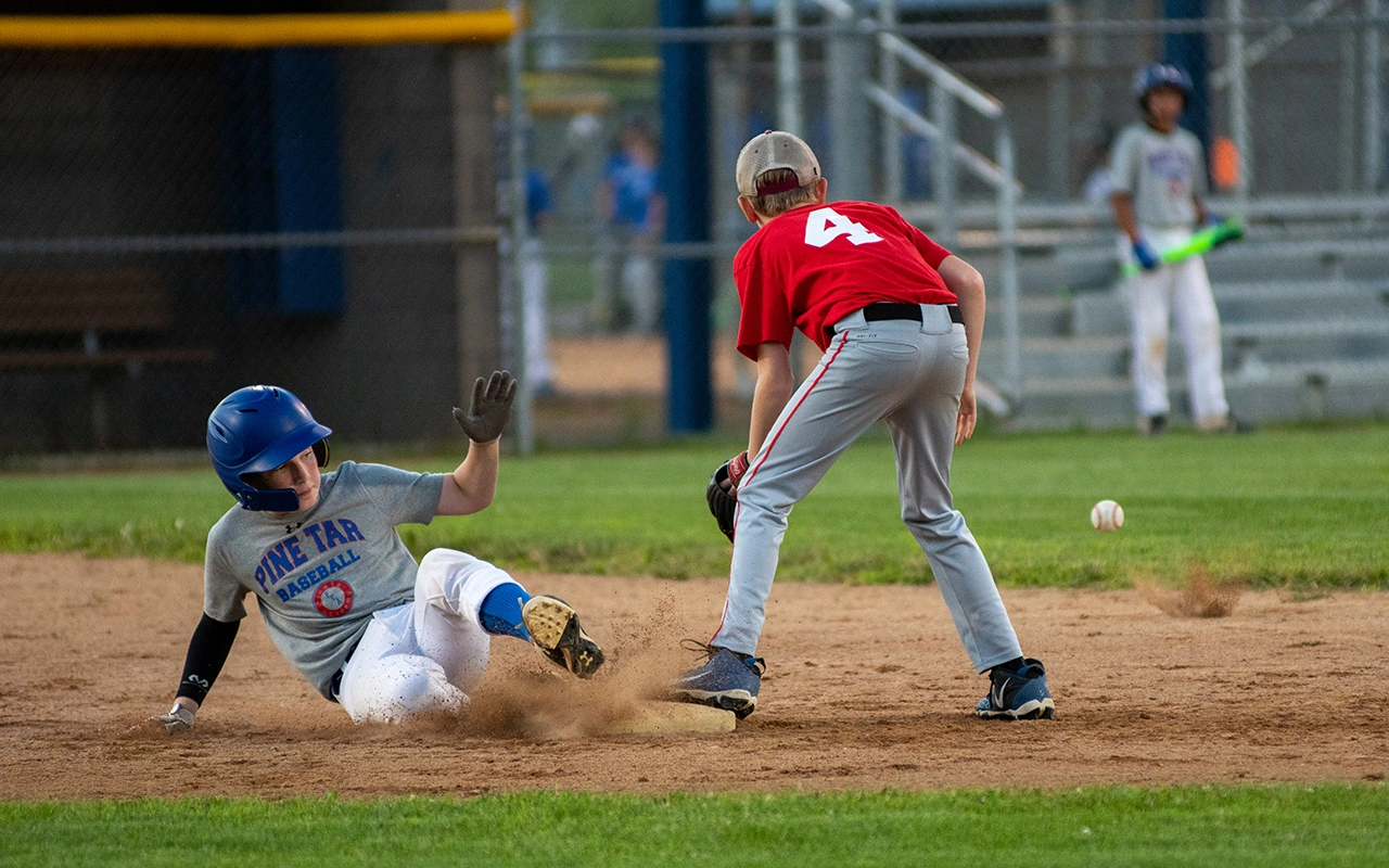 Youth travel baseball player slides into second base as fielder reaches for the throw during a Minnesota game day